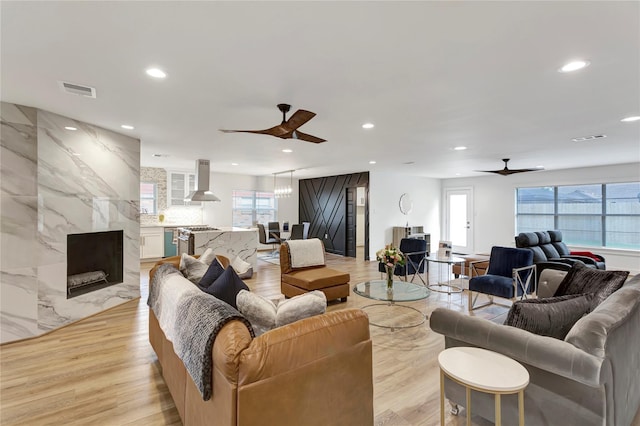 living room with ceiling fan, a high end fireplace, light wood-type flooring, and plenty of natural light