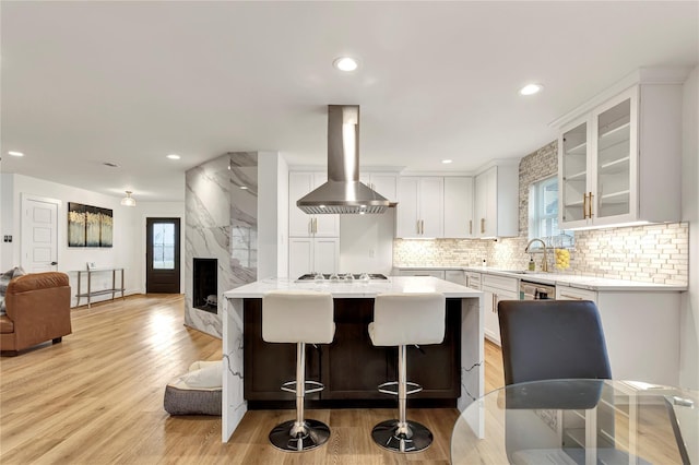 kitchen with appliances with stainless steel finishes, white cabinetry, a fireplace, island exhaust hood, and decorative backsplash