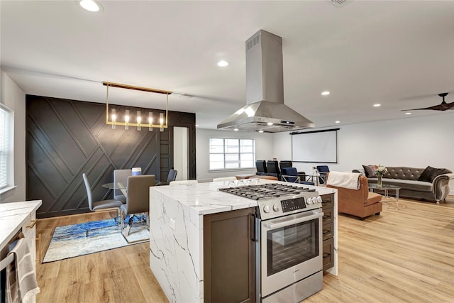 kitchen featuring stainless steel gas range oven, island exhaust hood, light hardwood / wood-style floors, and decorative light fixtures