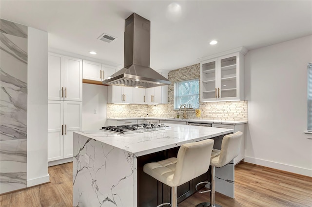 kitchen with stainless steel gas cooktop, light stone counters, a kitchen island, island exhaust hood, and white cabinets