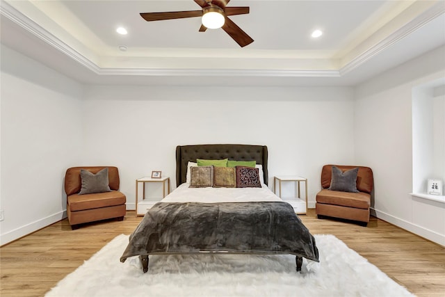 bedroom featuring light hardwood / wood-style flooring, ceiling fan, and a tray ceiling