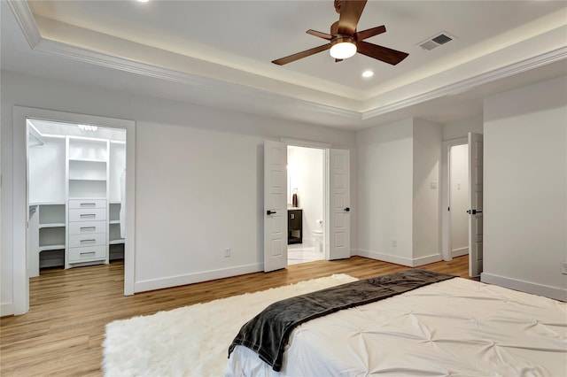 bedroom featuring a spacious closet, light hardwood / wood-style flooring, a raised ceiling, and ensuite bathroom