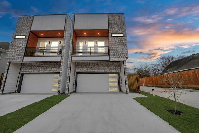 contemporary house with an attached garage, a balcony, brick siding, fence, and driveway