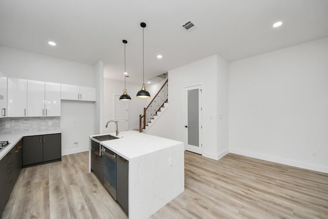 kitchen featuring hanging light fixtures, stainless steel dishwasher, a kitchen island with sink, white cabinetry, and a sink