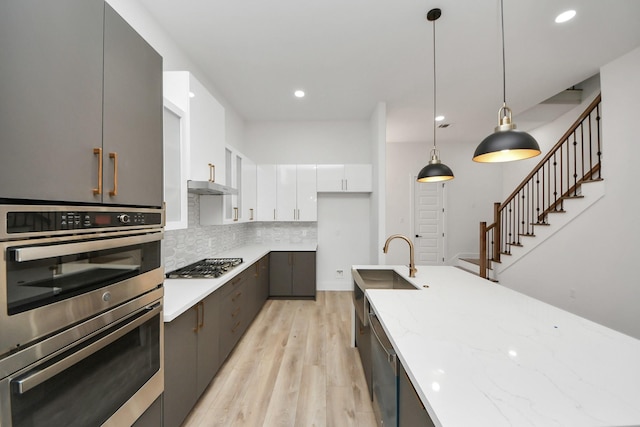 kitchen with modern cabinets, appliances with stainless steel finishes, under cabinet range hood, white cabinetry, and pendant lighting