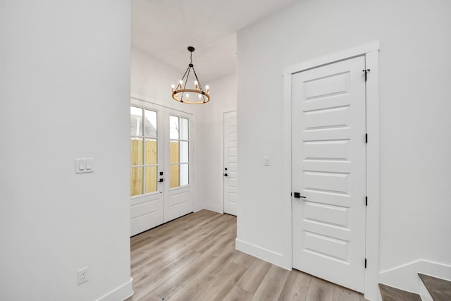 foyer entrance with light wood-type flooring, baseboards, and an inviting chandelier