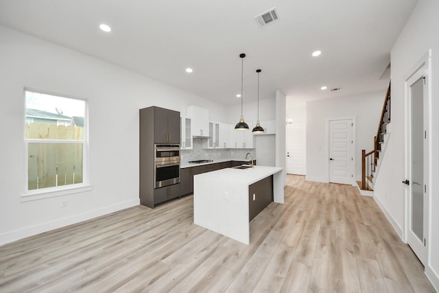 kitchen with pendant lighting, a center island with sink, light countertops, visible vents, and modern cabinets