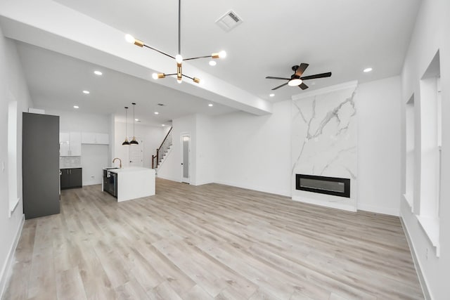 unfurnished living room with stairway, a fireplace, visible vents, and light wood-style floors