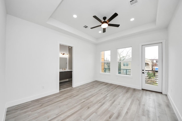 unfurnished room with light wood-style floors, a tray ceiling, and visible vents