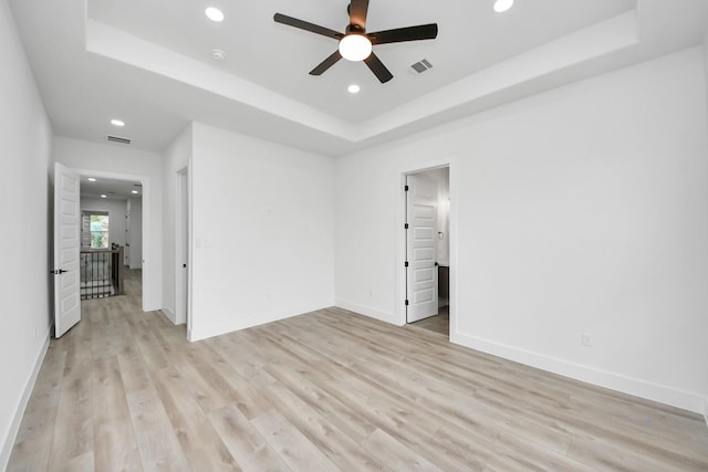 unfurnished room featuring a tray ceiling, light wood-type flooring, visible vents, and recessed lighting