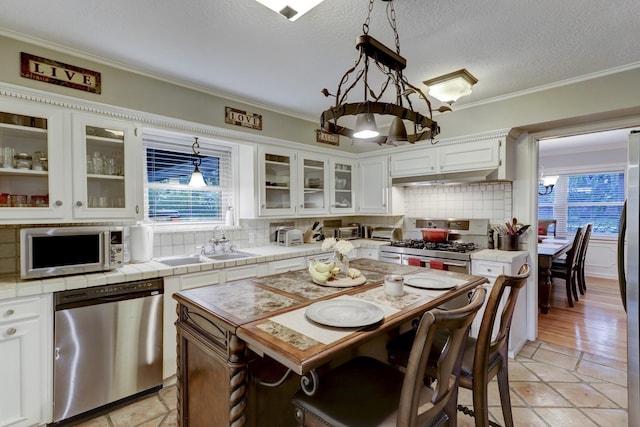 kitchen featuring appliances with stainless steel finishes, white cabinetry, a center island, tasteful backsplash, and tile counters