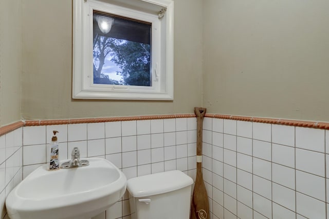 bathroom with toilet, sink, and tile walls