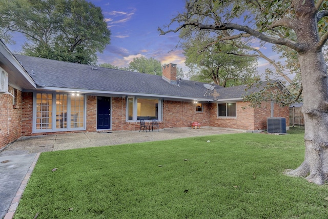 back house at dusk with central AC unit, a patio area, and a lawn