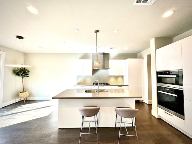 kitchen featuring sink, decorative light fixtures, white cabinets, and a center island with sink