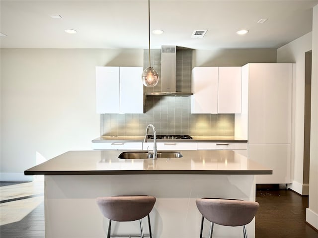 kitchen with white cabinets, a center island with sink, and wall chimney range hood