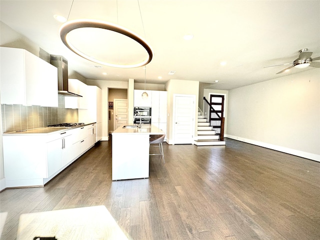 kitchen with hanging light fixtures, wall chimney range hood, white cabinets, and stainless steel appliances