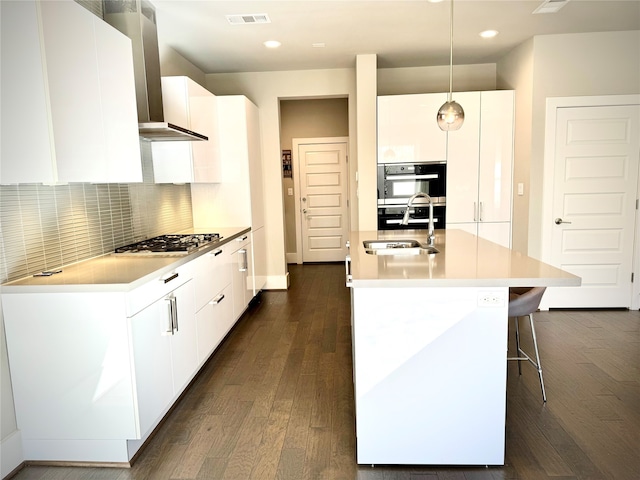 kitchen featuring pendant lighting, double oven, white cabinets, stainless steel gas cooktop, and a center island with sink