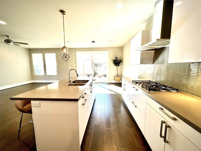 kitchen featuring sink, a center island with sink, wall chimney range hood, stainless steel gas stovetop, and white cabinets