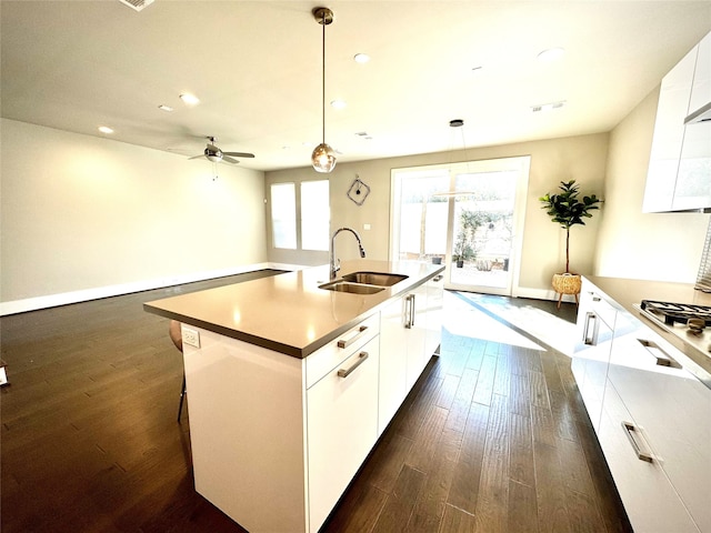 kitchen with dark hardwood / wood-style floors, sink, white cabinets, hanging light fixtures, and a center island with sink