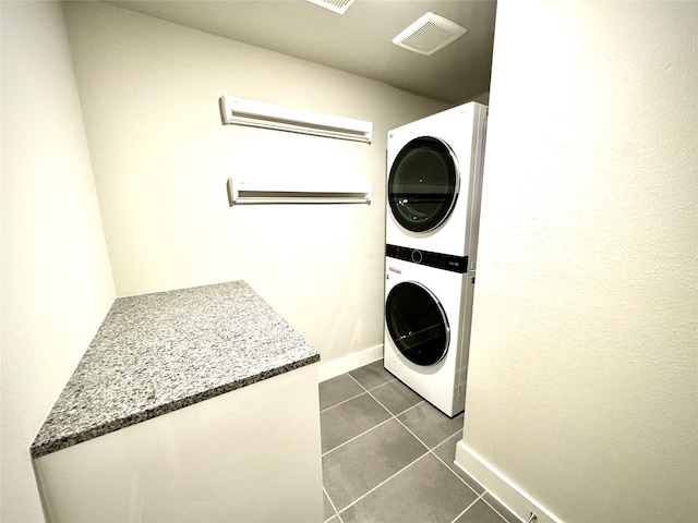 washroom featuring stacked washer / drying machine and dark tile patterned floors