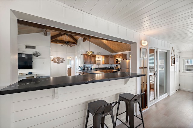 kitchen featuring stainless steel refrigerator, lofted ceiling with beams, a kitchen bar, wooden ceiling, and kitchen peninsula