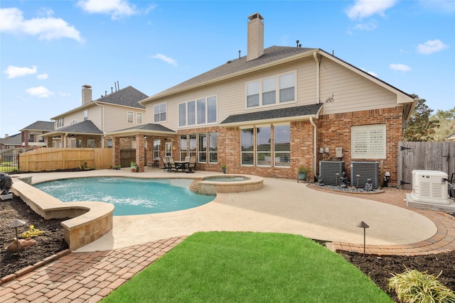 rear view of house featuring brick siding, fence, a pool with connected hot tub, a chimney, and a patio area