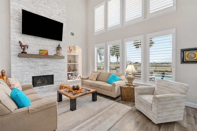 living area featuring a fireplace, visible vents, a towering ceiling, wood finished floors, and baseboards