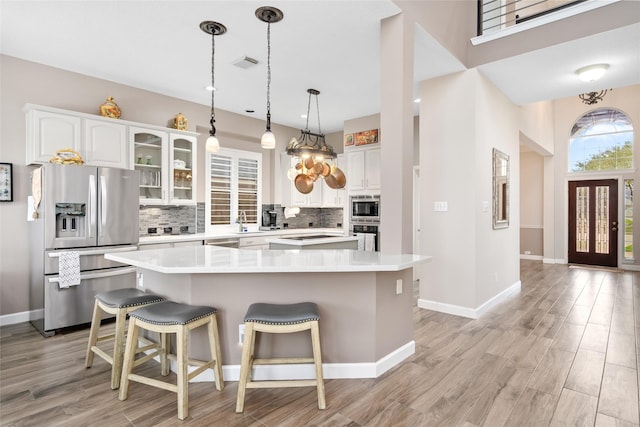 kitchen with appliances with stainless steel finishes, light countertops, glass insert cabinets, and white cabinetry