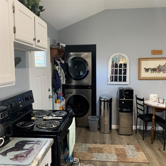 kitchen featuring black electric range oven, vaulted ceiling, light hardwood / wood-style flooring, stacked washing maching and dryer, and white cabinets