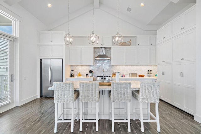 kitchen featuring white cabinets, a center island with sink, stainless steel fridge, and wall chimney exhaust hood