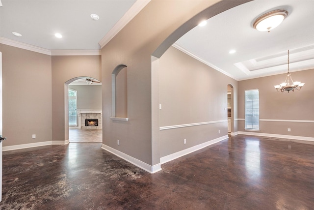 unfurnished room featuring crown molding, a tray ceiling, a fireplace, and a notable chandelier