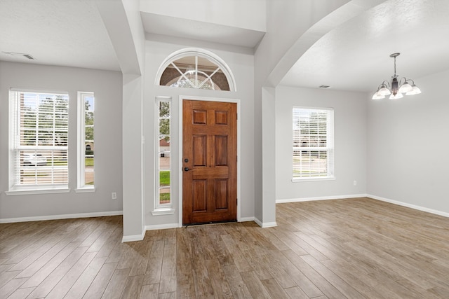 entryway with a textured ceiling, a notable chandelier, and light hardwood / wood-style floors