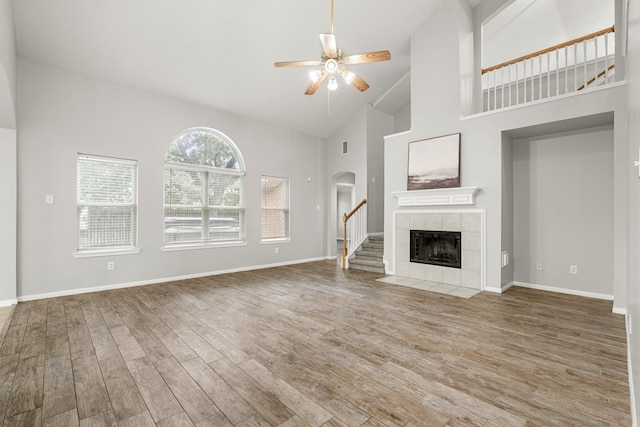 unfurnished living room featuring wood-type flooring, high vaulted ceiling, a tile fireplace, and ceiling fan