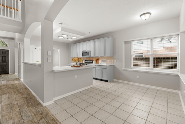 kitchen with gray cabinetry, stainless steel appliances, tasteful backsplash, light hardwood / wood-style floors, and kitchen peninsula