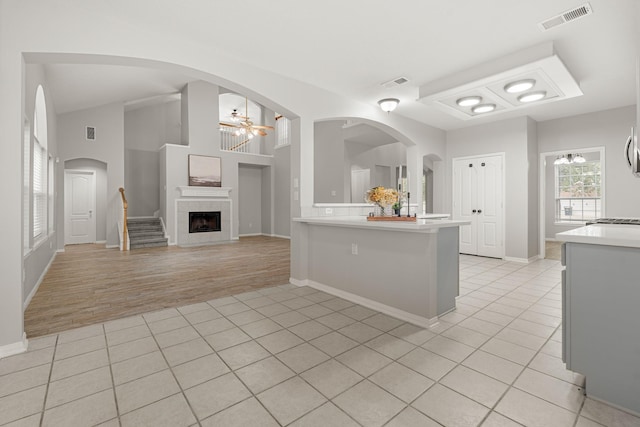 kitchen with light tile patterned flooring, vaulted ceiling, a tiled fireplace, ceiling fan, and kitchen peninsula