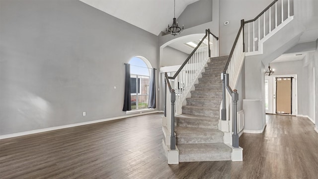 stairs with high vaulted ceiling, hardwood / wood-style floors, and a notable chandelier