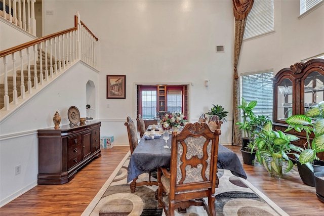 dining room featuring a towering ceiling, a healthy amount of sunlight, and light hardwood / wood-style floors