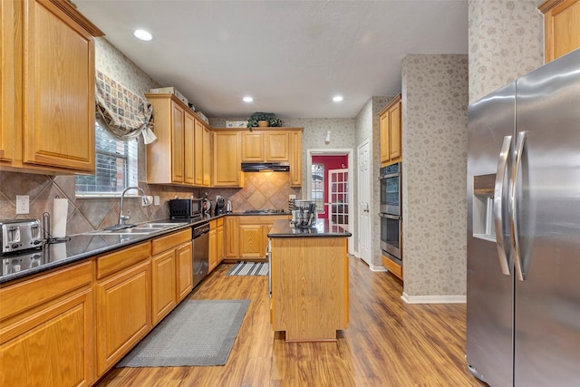 kitchen featuring sink, backsplash, a center island, stainless steel appliances, and light wood-type flooring