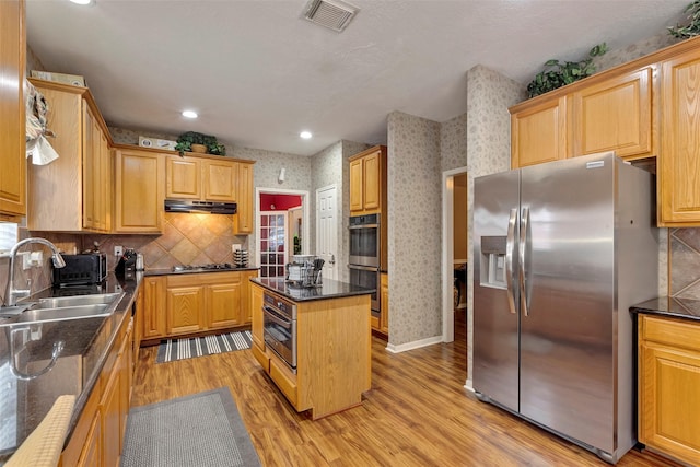 kitchen featuring sink, dark stone countertops, appliances with stainless steel finishes, a kitchen island, and light hardwood / wood-style floors