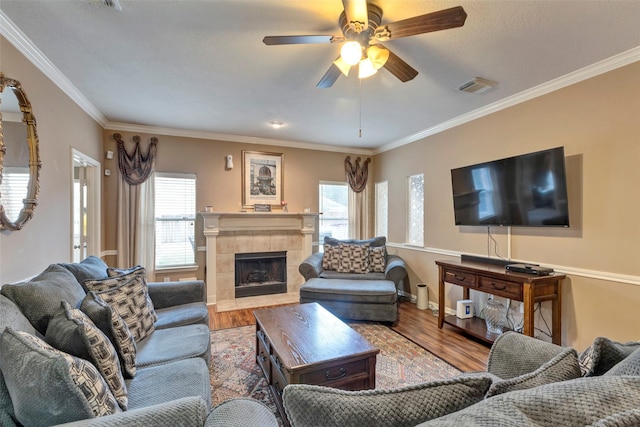 living room with crown molding, a healthy amount of sunlight, a tile fireplace, and wood-type flooring