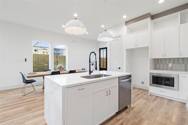 kitchen featuring white cabinetry, dishwasher, an island with sink, and decorative light fixtures