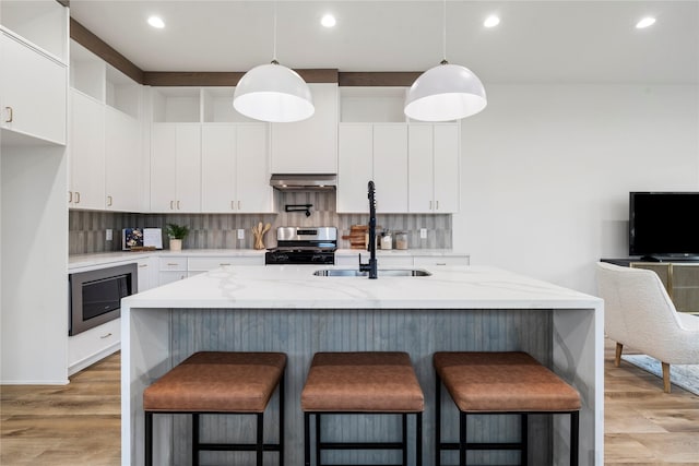 kitchen featuring white cabinetry, hanging light fixtures, an island with sink, stainless steel range oven, and built in microwave