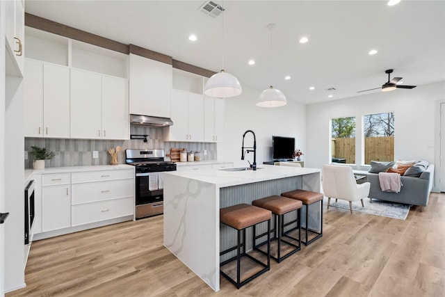 kitchen featuring a kitchen island with sink, stainless steel range with gas cooktop, sink, and white cabinets