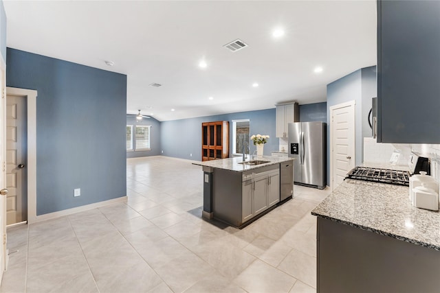 kitchen featuring ceiling fan, appliances with stainless steel finishes, a kitchen island with sink, gray cabinetry, and light stone countertops