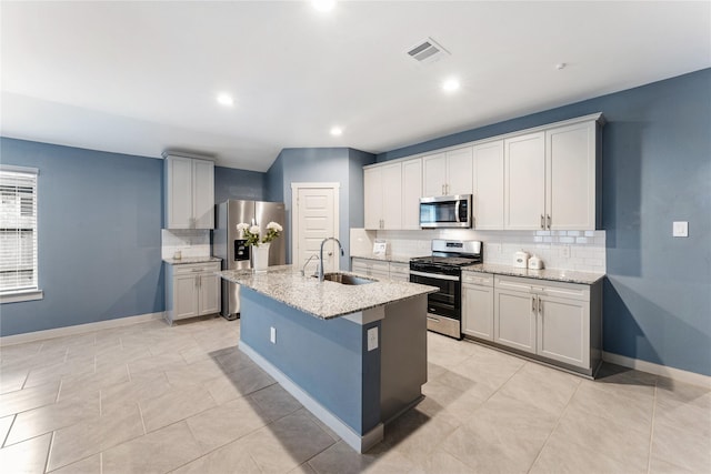 kitchen featuring a kitchen island with sink, sink, stainless steel appliances, and light stone countertops