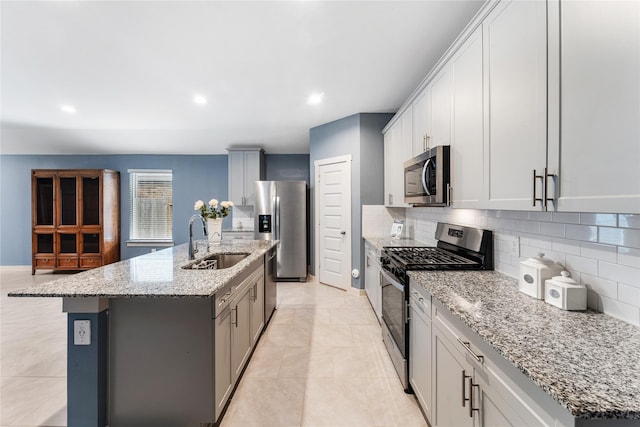 kitchen with appliances with stainless steel finishes, sink, decorative backsplash, a kitchen island with sink, and light stone counters