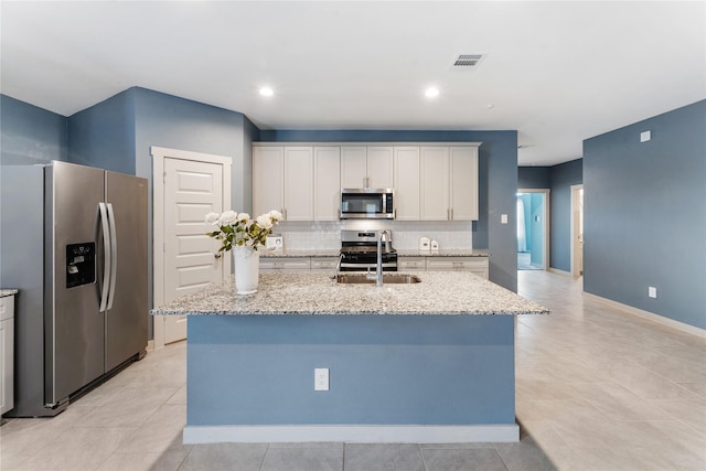 kitchen with appliances with stainless steel finishes, sink, white cabinets, a kitchen island with sink, and light stone counters