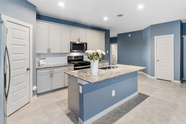 kitchen featuring appliances with stainless steel finishes, an island with sink, sink, backsplash, and light stone countertops