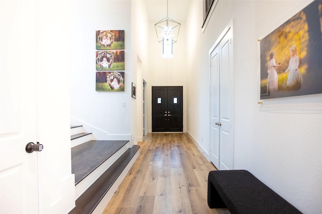 doorway featuring a towering ceiling, a chandelier, and light hardwood / wood-style flooring