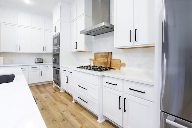 kitchen with white cabinetry, appliances with stainless steel finishes, light hardwood / wood-style floors, and wall chimney range hood